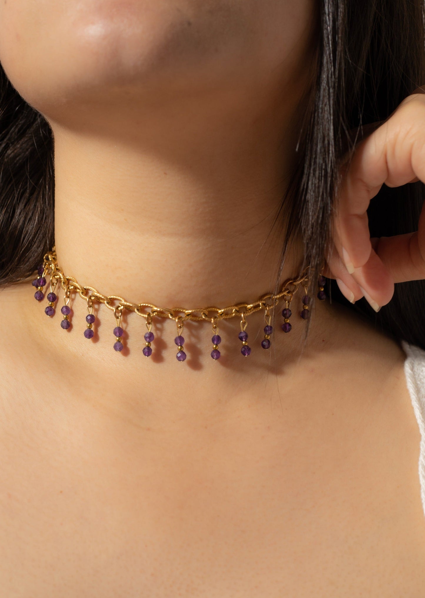 Bijoux ras de cou de couleur dorée avec perles tombantes de couleur violette sur une femme de peau blanche