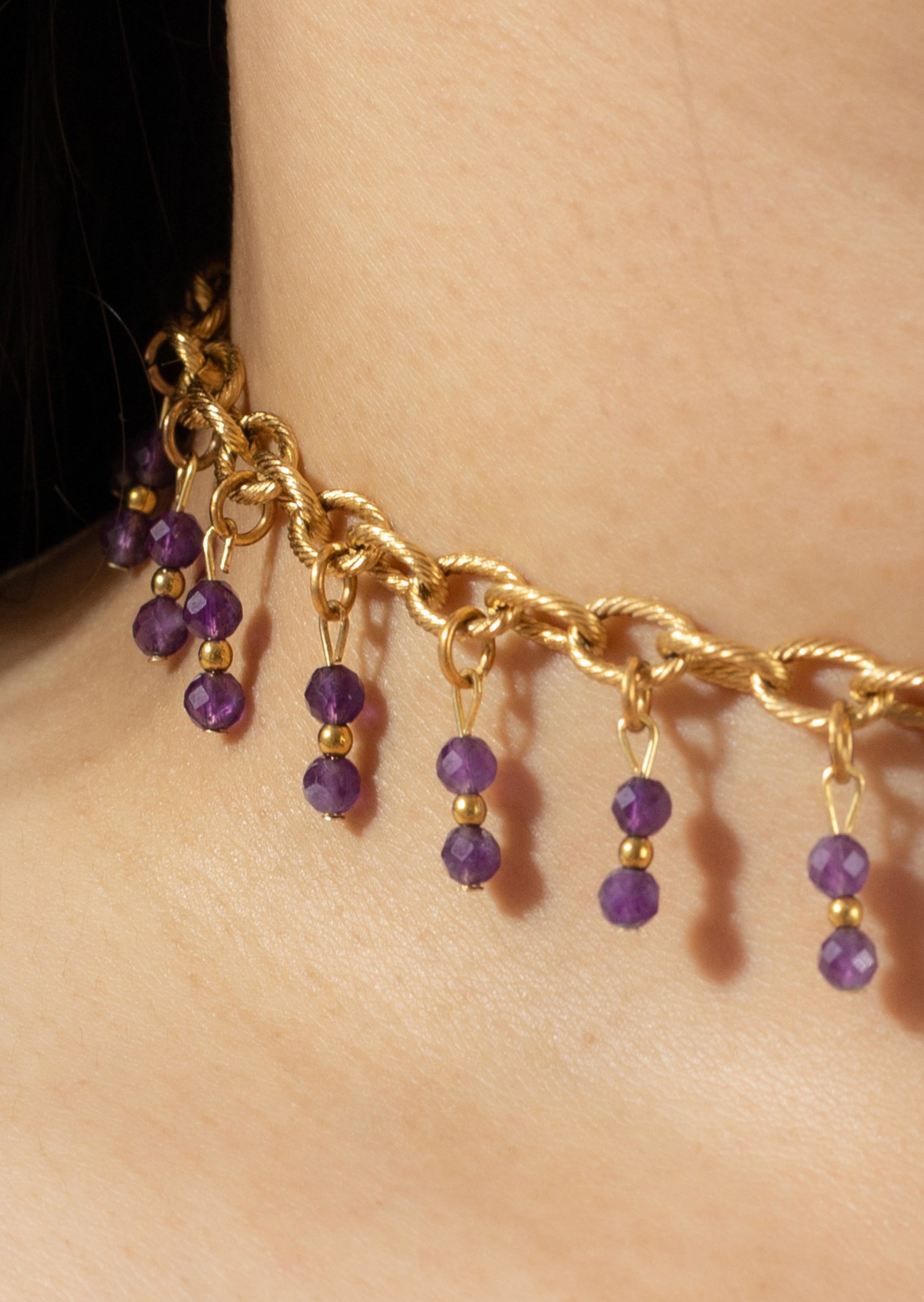 Bijoux ras de cou de couleur dorée avec perles tombantes de couleur violette sur une femme de peau blanche