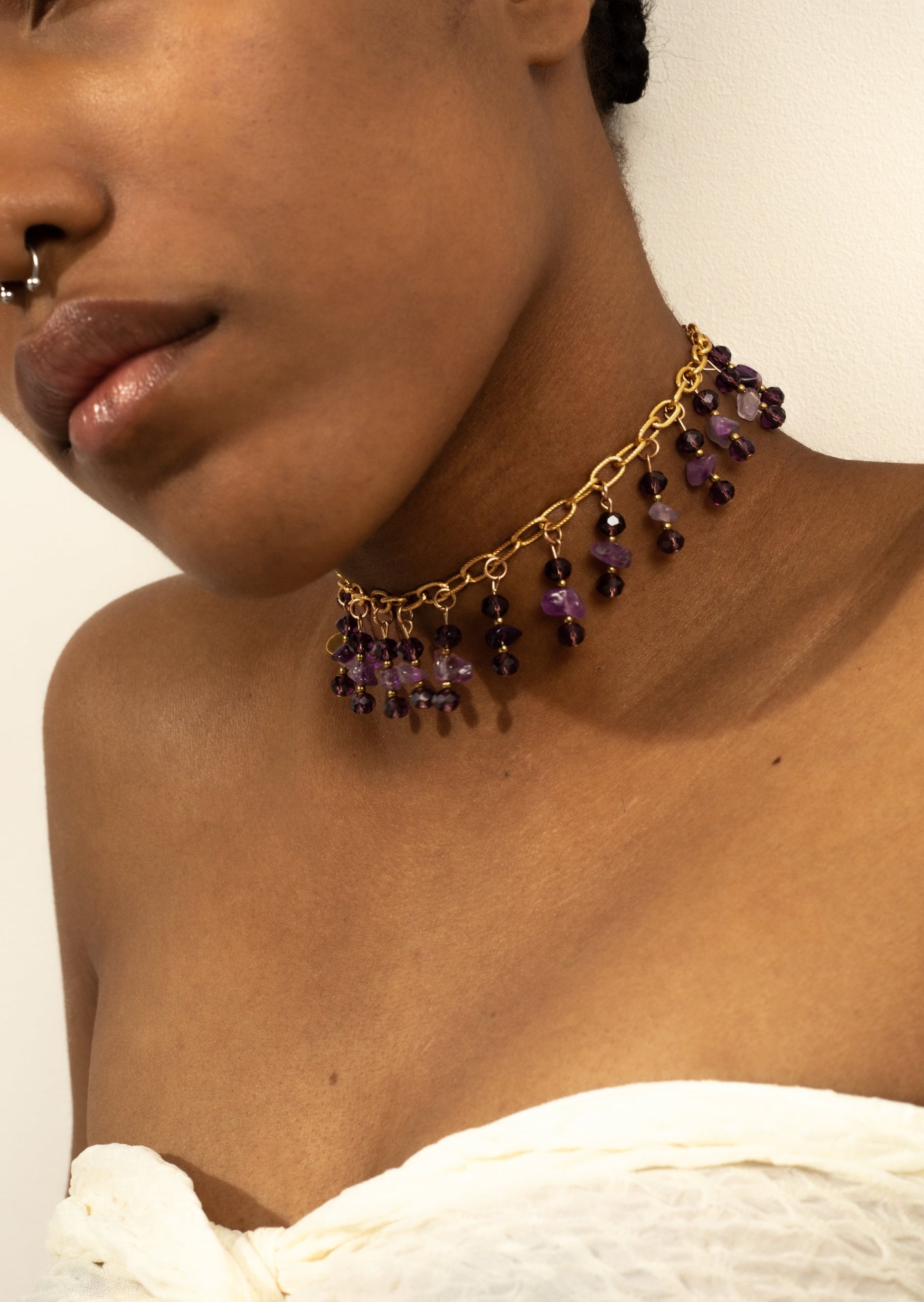 Bijoux ras de cou doré avec des perles violettes tombante sur une femme de  peau mate