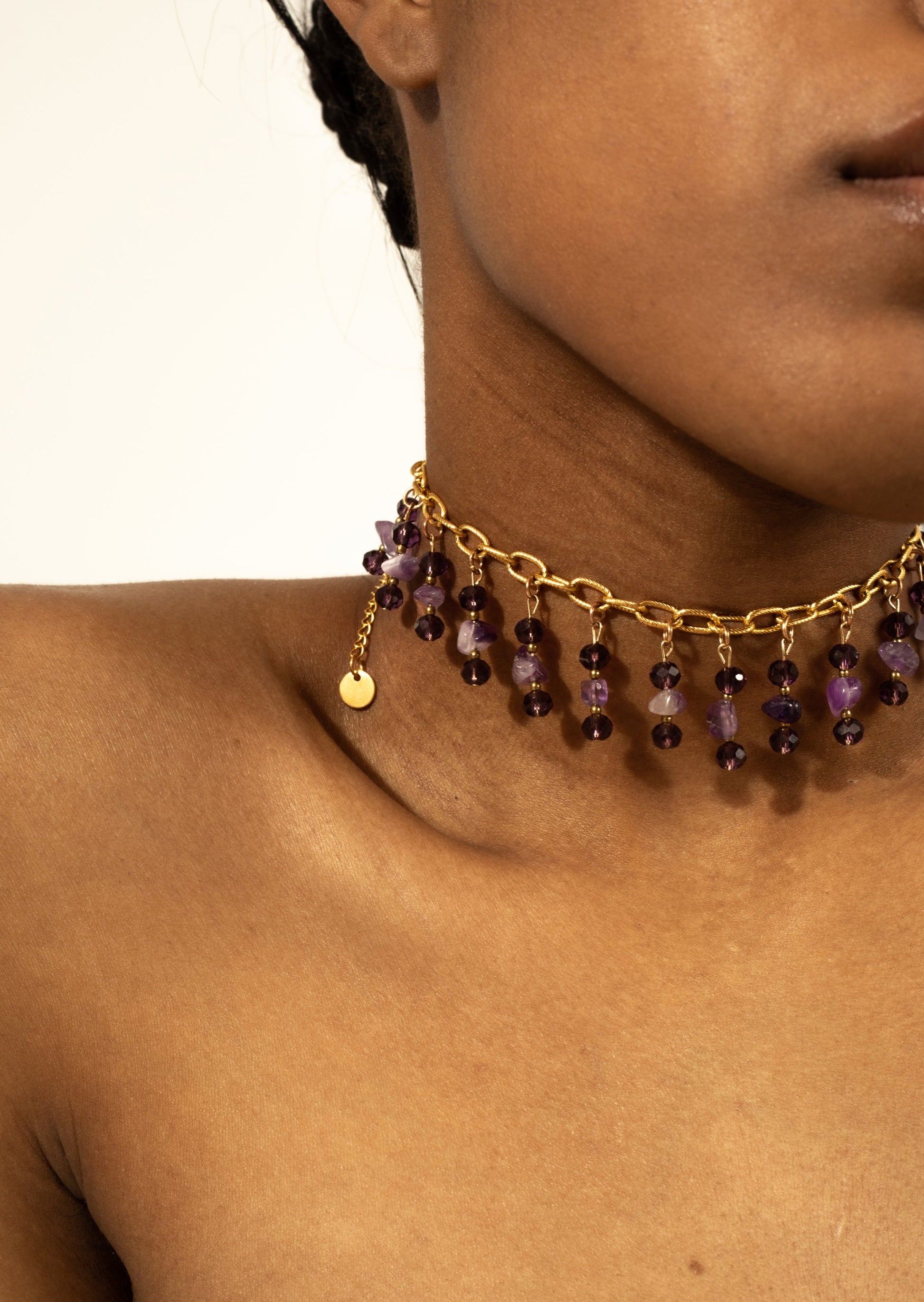 Bijoux ras de cou doré avec des perles violettes tombante sur une femme de  peau mate