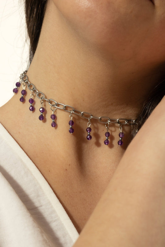 Bijoux ras de cou de couleur grise avec perles tombantes de couleur violette sur une femme de peau blanche