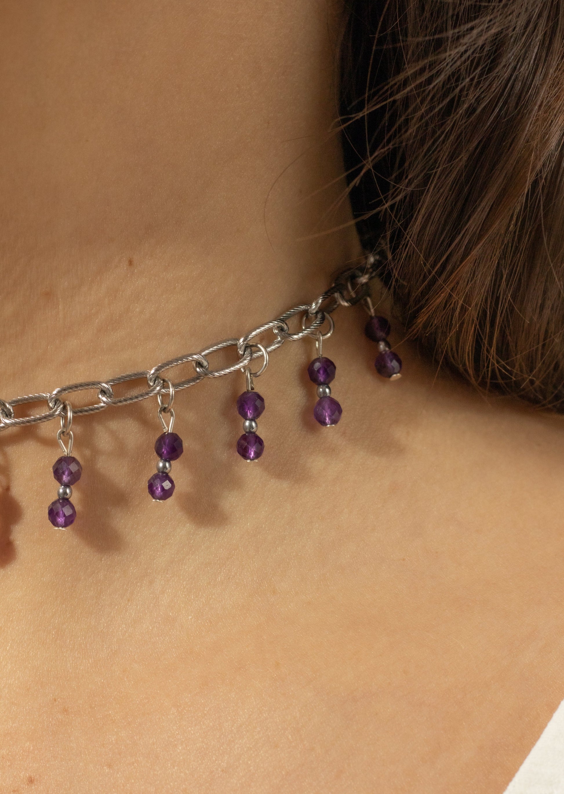 Bijoux ras de cou de couleur grise avec perles tombantes de couleur violette sur une femme de peau blanche